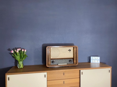 Blaue Lehmputzwand davor ein Sideboard mit einem antiken Radio und einer Blumenvase mit Tulpen